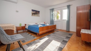 A bedroom with a bed, a chair, a desk, a window with curtains, and a wall-mounted air conditioner. - Apartment Ivana (Omis)