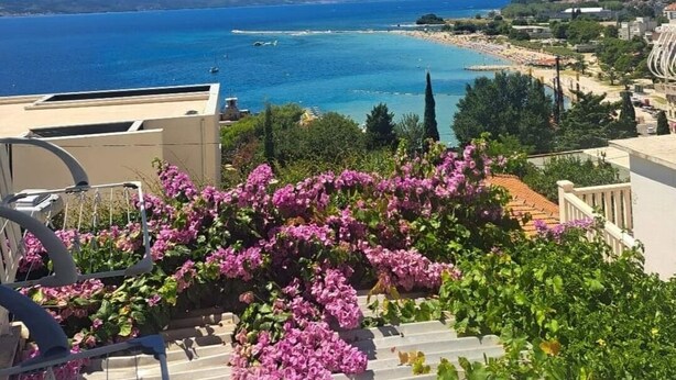 A balcony with a view of the sea, a beach, and a cityscape in the distance. - Apartment Ivana (Omis)
