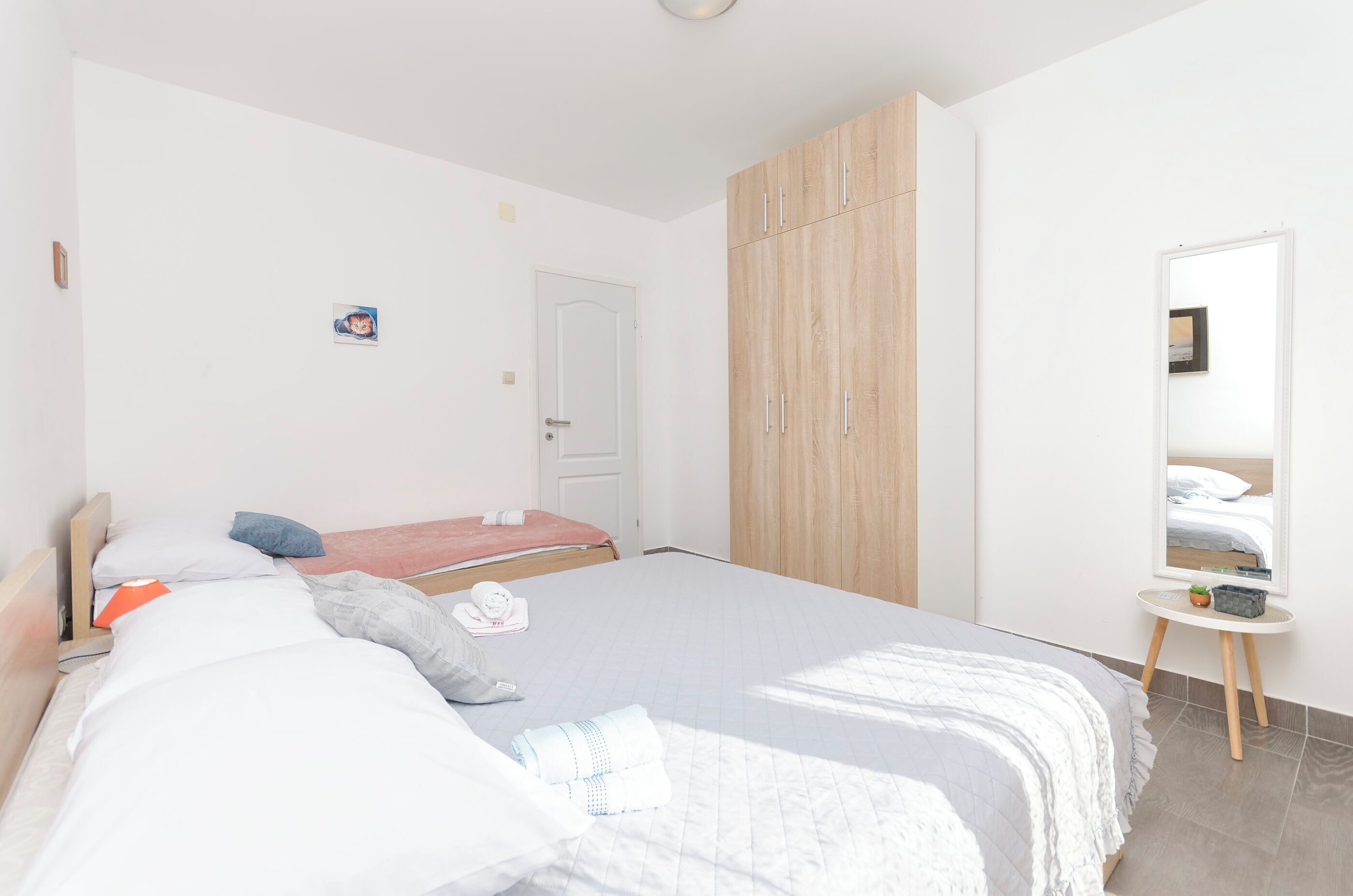 A bedroom with a large bed, a wardrobe, a bedside table, and a mirror.