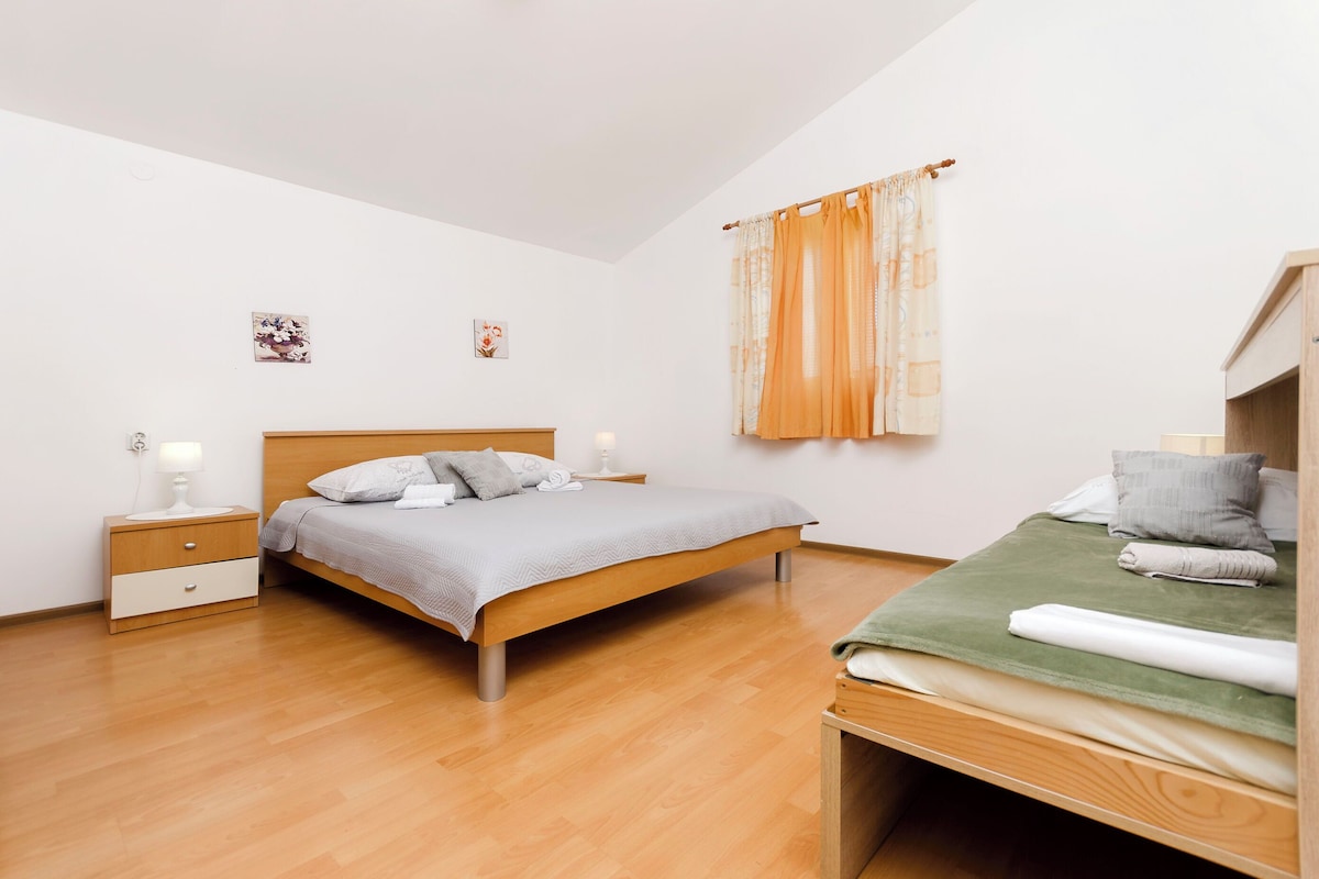 A bedroom with a wooden bed, a nightstand, a bedside table, and a window with curtains.