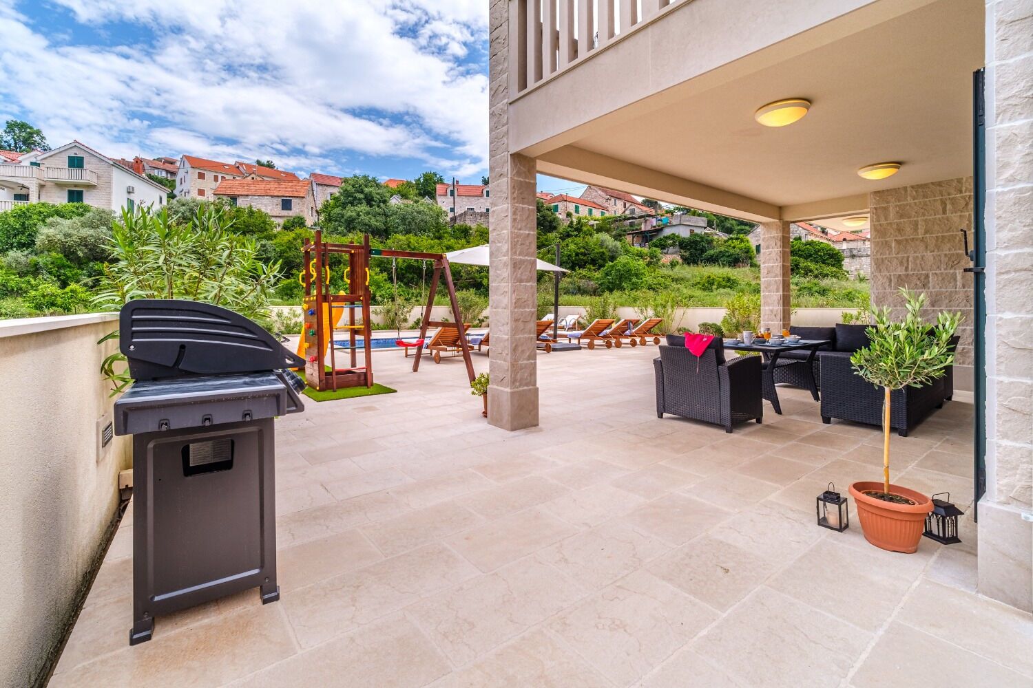 Une terrasse extérieure équipée d’un barbecue, de meubles de jardin et d’un espace de jeux pour enfants.