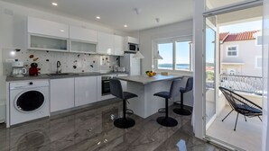 Une cuisine moderne avec des meubles blancs, un lave-linge encastré et un grand îlot central doté de tabourets de bar.
