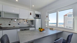 Une cuisine moderne avec des meubles blancs, un plan de travail en granit et une vue sur la plage grâce à de grandes fenêtres.