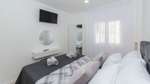 Une chambre à coucher moderne, avec un lit, une table de chevet, un miroir et un téléviseur fixé au mur.