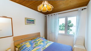 Une chambre avec un plafond en bois, un lit recouvert d’une courtepointe colorée, une table de chevet avec une lampe, une fenêtre avec des rideaux et un tableau encadré accroché au mur.