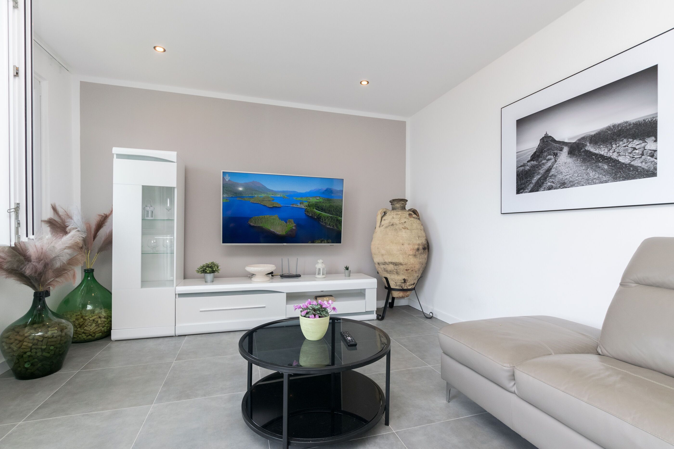 A modern living room with a flat-screen TV, a sofa, a coffee table, and decorative items including vases and a large vase.