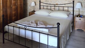 A bedroom with a stone wall, wooden wardrobe, metal bed frame, and bedside lamps. - Apartments Studio Zaton (Nin)