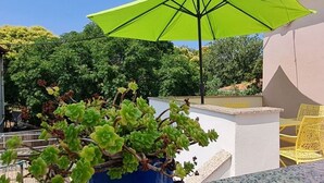 A balcony with a green umbrella, yellow chairs, and a potted plant. - Apartments Studio Zaton (Nin)