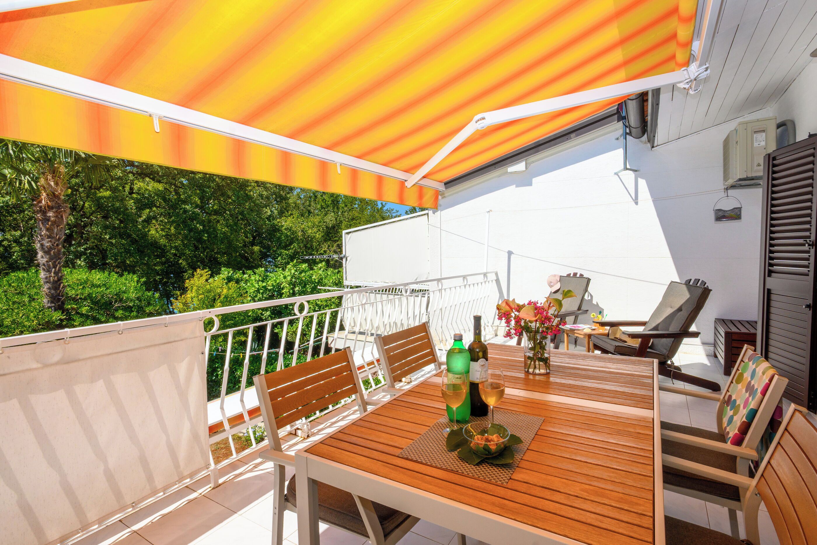 Un patio exterior con una mesa y sillas de madera, y una zona cubierta con un toldo a rayas.