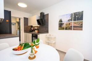 A modern kitchen with white cabinets, a black range hood, and a dining area with a white table and chairs. - Apartments Rosuje (Omisalj)