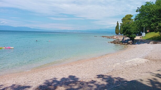 Une plage avec une eau claire, un rivage de galets et des arbres.