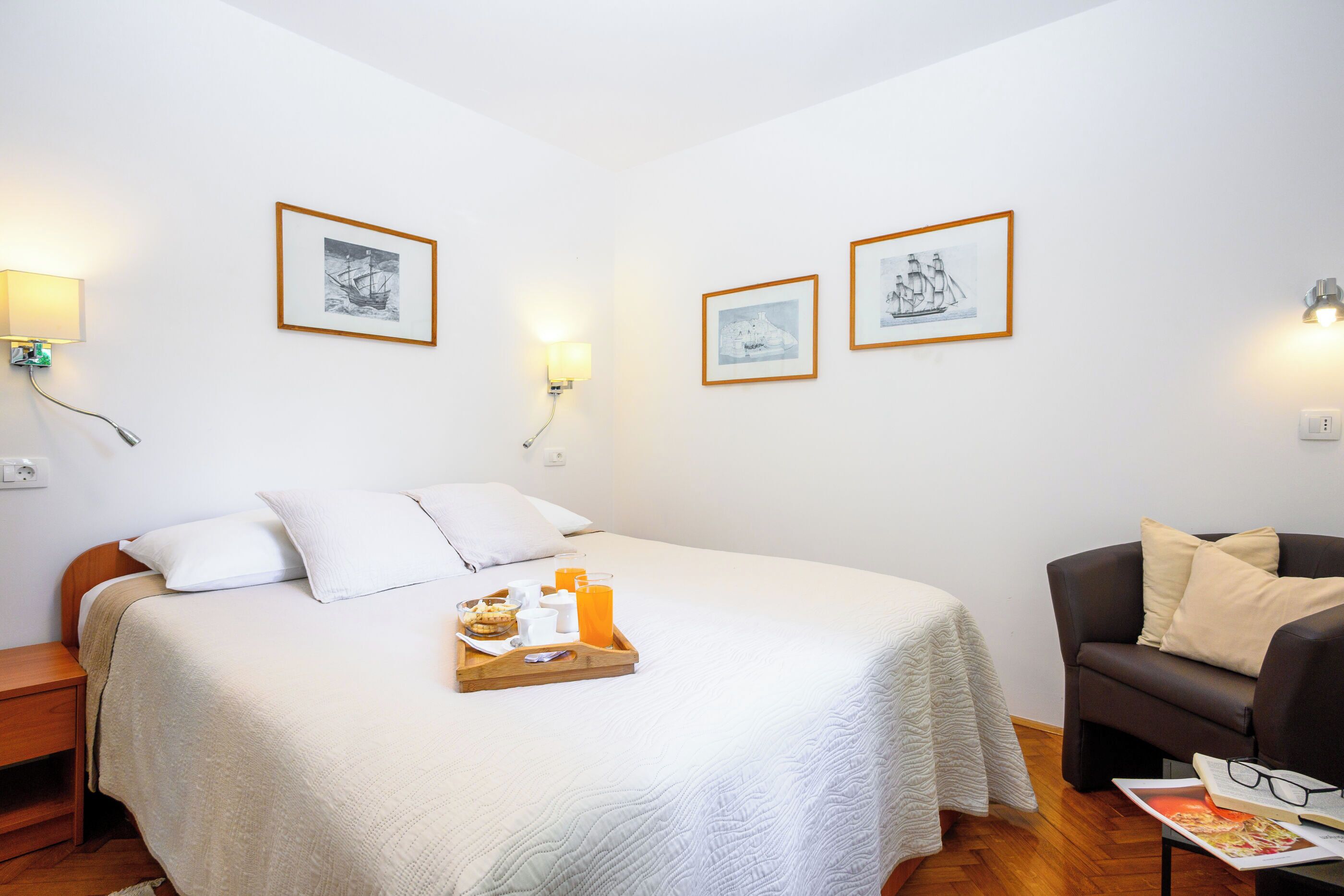 A hotel room with a bed, a bedside table, a chair, and two framed pictures on the wall.