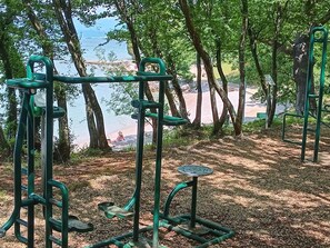Outdoor exercise equipment near a body of water, surrounded by trees. - Apartments Rosuje (Omisalj)