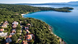 An aerial view of a coastal area with residential buildings, a beach, and a large body of water. - Apartments Rosuje (Omisalj)