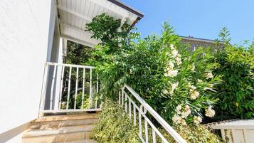 A staircase leading to a white building with a white railing, surrounded by lush greenery and flowering plants.