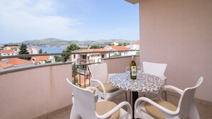 Ein Balkon mit Tisch und Stühlen, einer Weinflasche und Blick auf das Meer und die Gebäude.