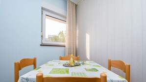 Una mesa de comedor con mantel verde y blanco, rodeada de sillas de madera, en una habitación con paredes azul claro y una ventana con cortina.
