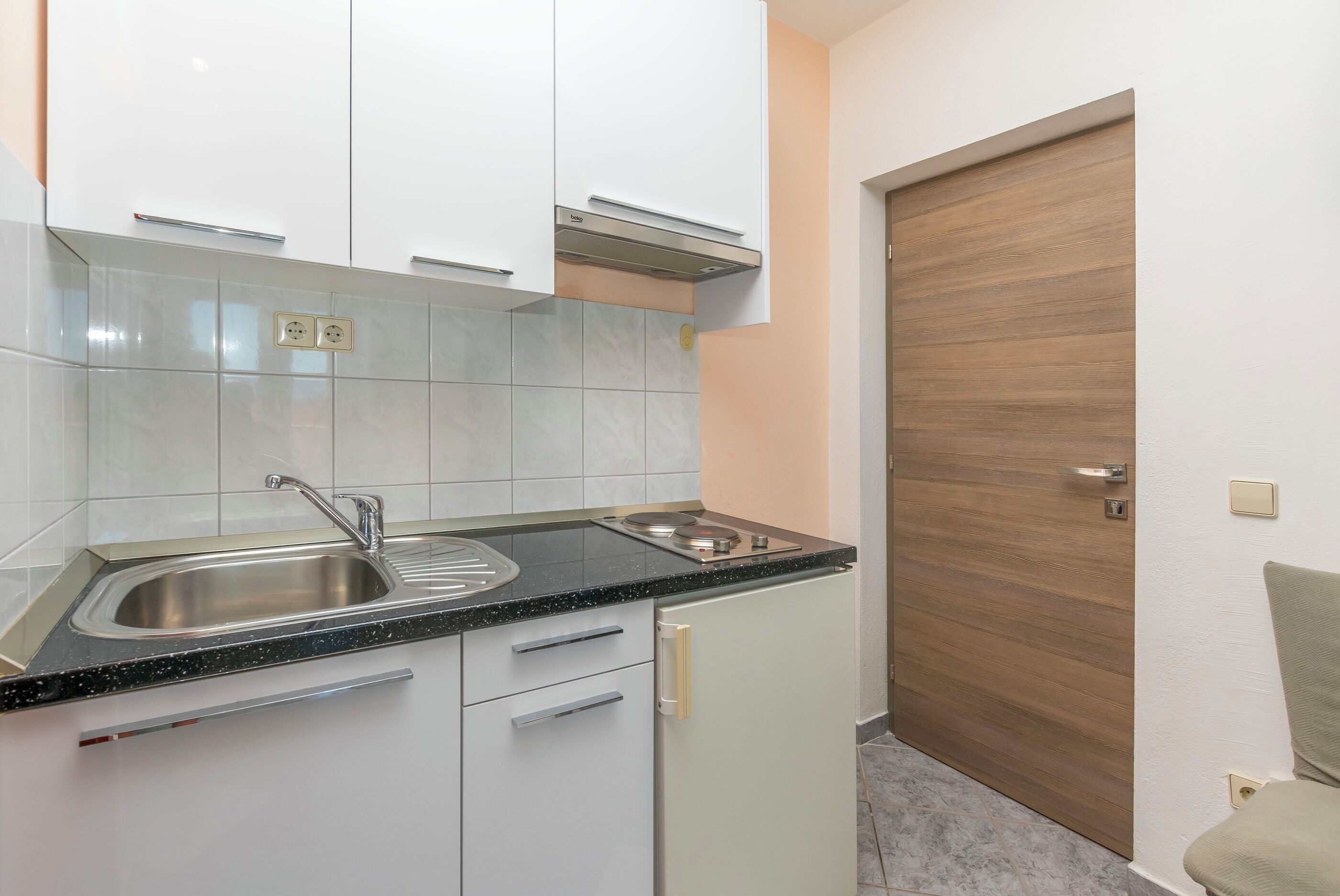 A kitchen with white cabinets, a black countertop, a stainless steel sink, and a wooden door.