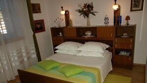 A neatly made bed with green and white bedding, wooden headboard, and bedside tables with decorative items. - Apartment Haus Franciska (Podgora)