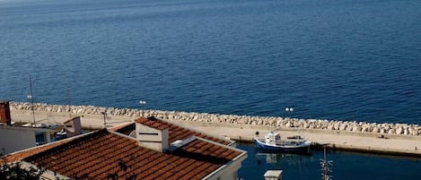 A coastal view with a marina, buildings with red-tiled roofs, and a clear blue sea.