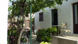 Un patio con una pérgola cubierta de parras, un edificio blanco con una ventana y mobiliario exterior.
