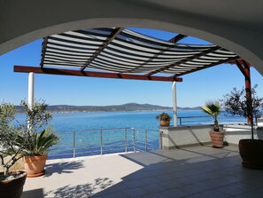 Un espacio al aire libre cubierto con vistas al mar, plantas en macetas y una barandilla metálica.