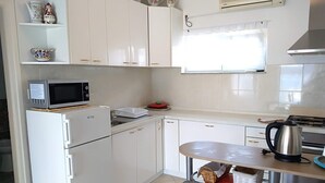 Una cocina compacta con gabinetes blancos, un microondas, un refrigerador, una estufa y un pequeño comedor con sillas.
