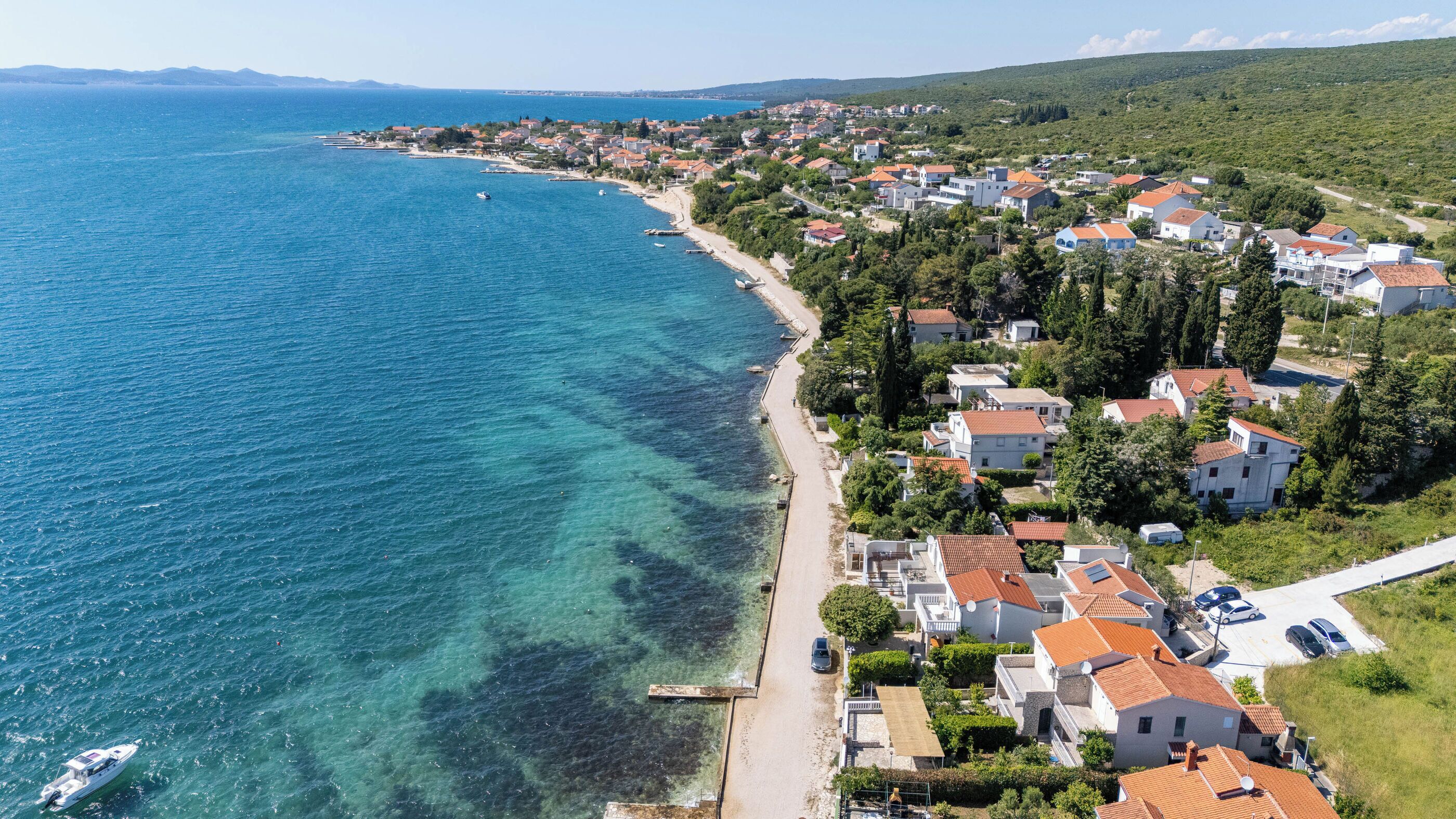 Vue aérienne d’une ville côtière avec une plage dégagée, des immeubles résidentiels et un quai pour bateaux.