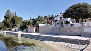 Una piscina cristalina con una pared de piedra y cerca blanca, rodeada de árboles y casas.