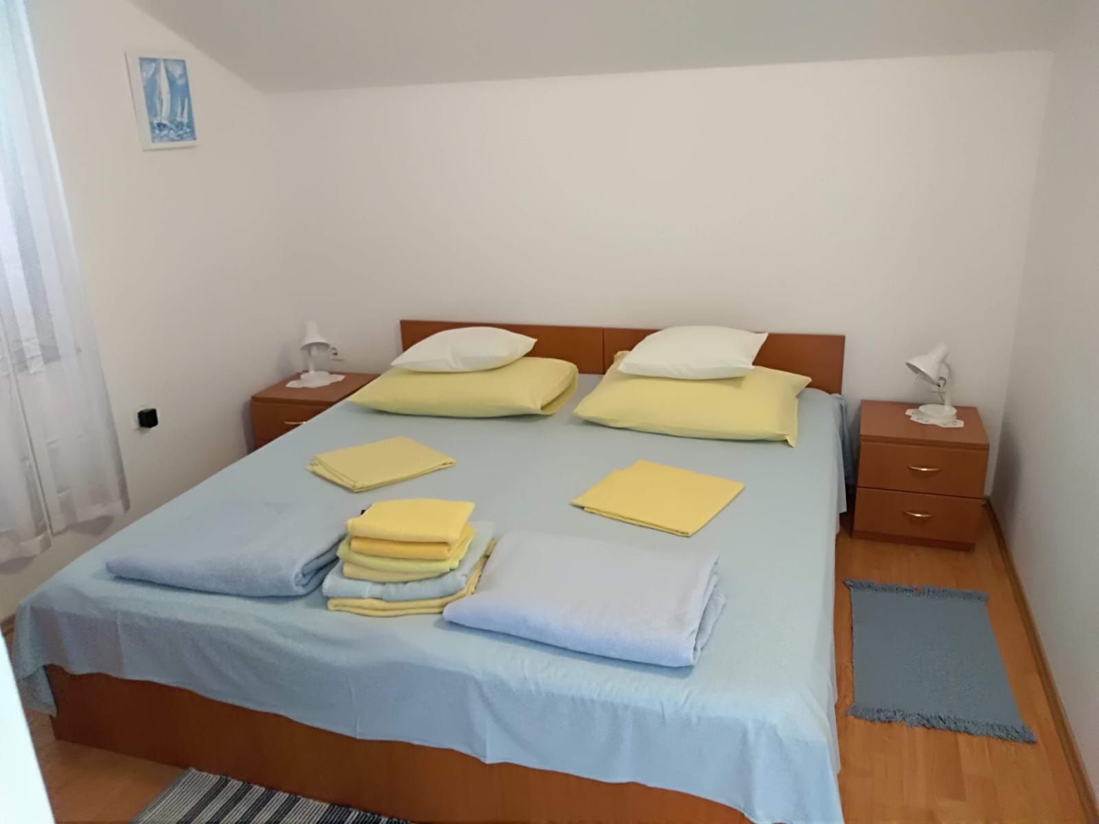 Un lit bien fait, avec du linge de lit bleu et jaune, deux tables de chevet avec des lampes et un petit tableau accroché au mur.