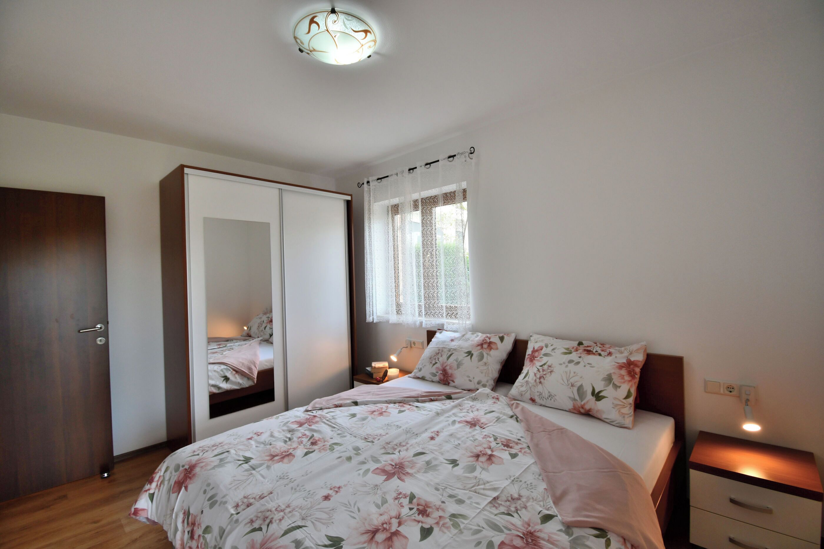 A bedroom with a bed, a wardrobe, a nightstand, and a window with a curtain.