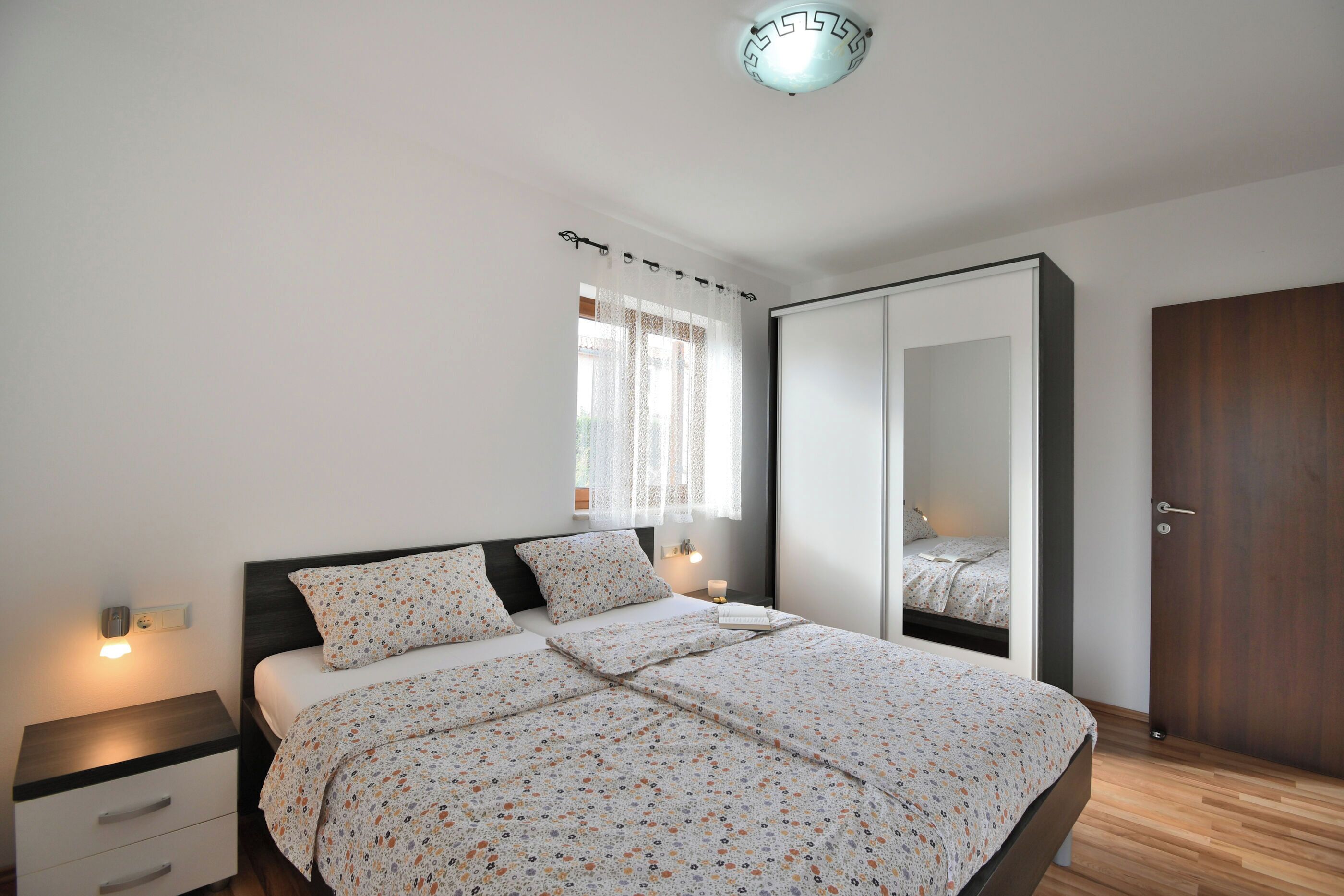 Ein Schlafzimmer mit Bett, Nachttischen, einem Kleiderschrank und einem Fenster mit Vorhängen.