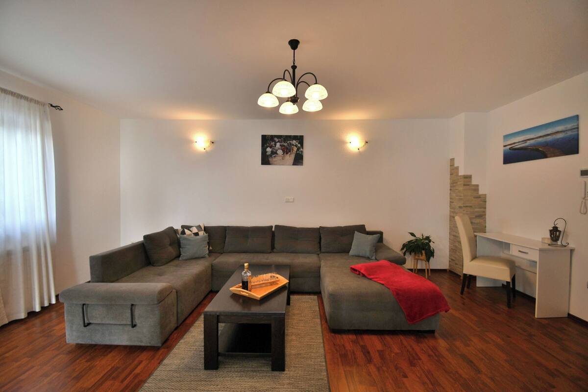 Un salon moderne comprenant un canapé d’angle, une table basse, un bureau et un fauteuil. Un escalier mène à un autre niveau.