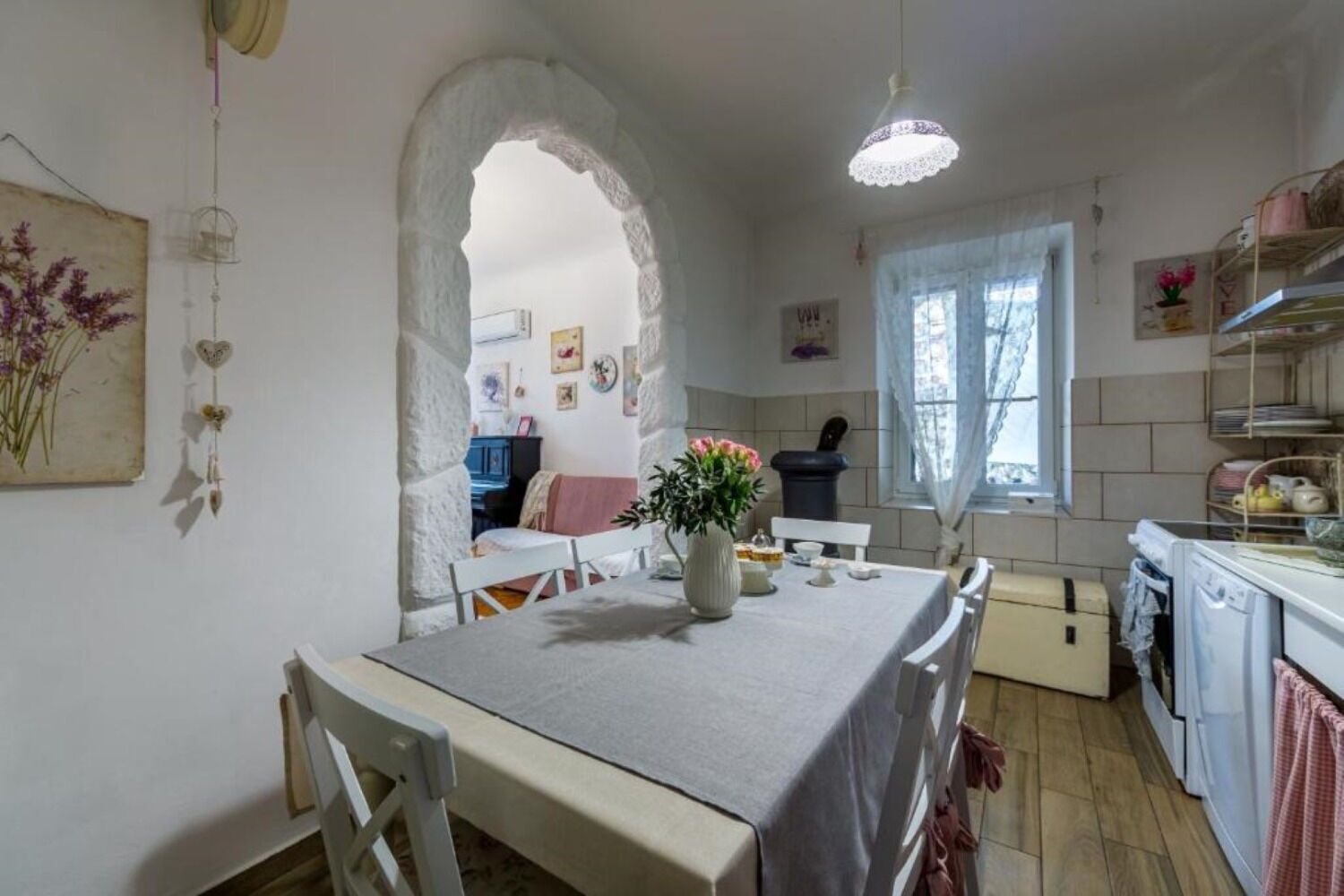 A cozy dining area with a table set for two, a vase with flowers, and a kitchen in the background.