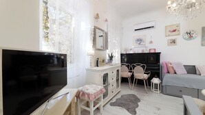 Un salon chaleureux avec un téléviseur, un canapé, un coin repas avec des chaises, une cheminée et un lustre.