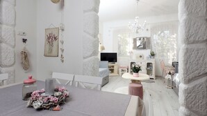 Une pièce chaleureuse et bien éclairée, avec une table à manger, des chaises, un téléviseur et un coin cuisine visible à travers une arche.