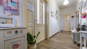 Un couloir avec un plancher en bois, une plante en pot et un tableau d’affichage recouvert de feuilles de papier.