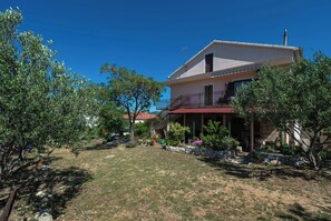 Ein zweistöckiges Haus mit Balkon, umgeben von einem Garten mit verschiedenen Pflanzen und Bäumen.