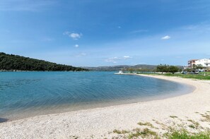 A beach with clear water, a boat, and a building with a balcony. - Apartments Saric (Sibenik)
