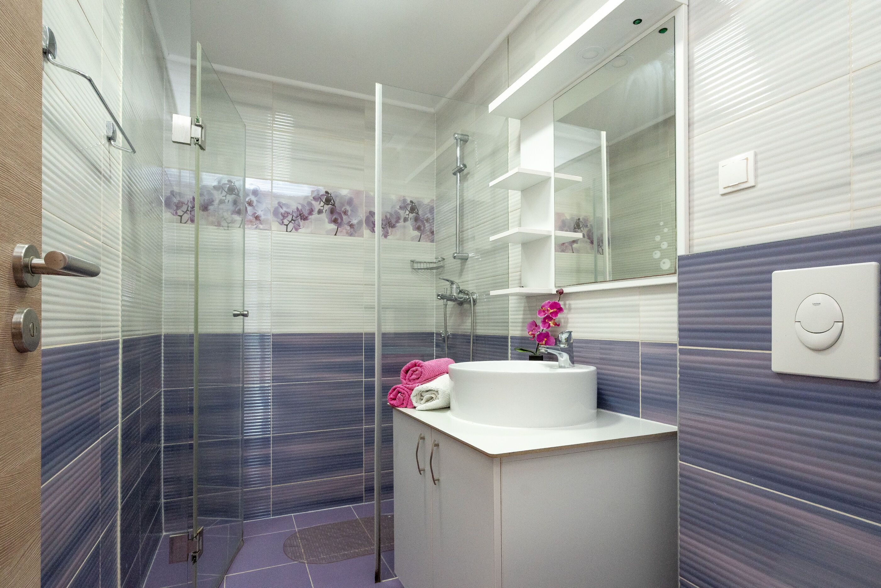 Un baño moderno con ducha de vidrio, un lavabo blanco y un espejo.