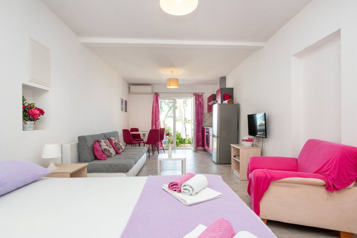 A hotel room with a bed, a sofa, a TV, a dining area, and a kitchen.