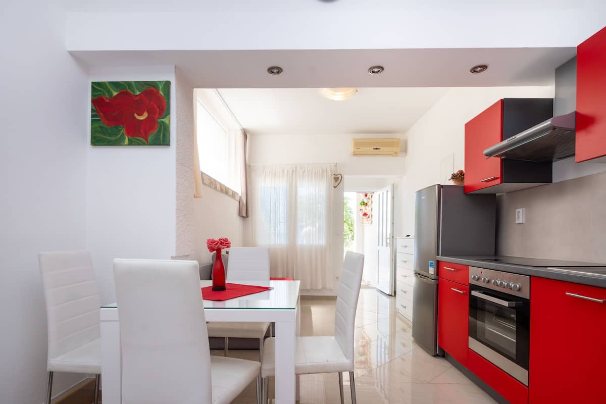 A modern kitchen with red cabinets, a stainless steel oven, and a dining area with white chairs and a glass table.