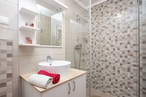Une salle de bain avec un lavabo blanc, une cabine de douche en verre et un mur de douche recouvert de carreaux.