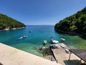 A coastal view with boats on clear water, a sandy beach, and a wooden structure with lounge chairs. - Apartments Villa Smokvina (Sucuraj)