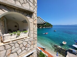 A stone building with a covered outdoor seating area overlooking a clear blue sea with boats. - Apartments Villa Smokvina (Sucuraj)