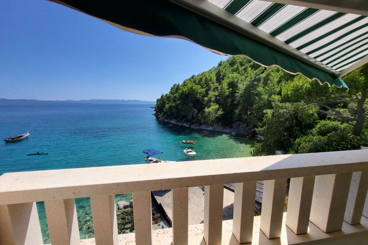 Ein Balkon mit Blick auf ein türkisblaues Meer, Boote und eine bewaldete Insel.