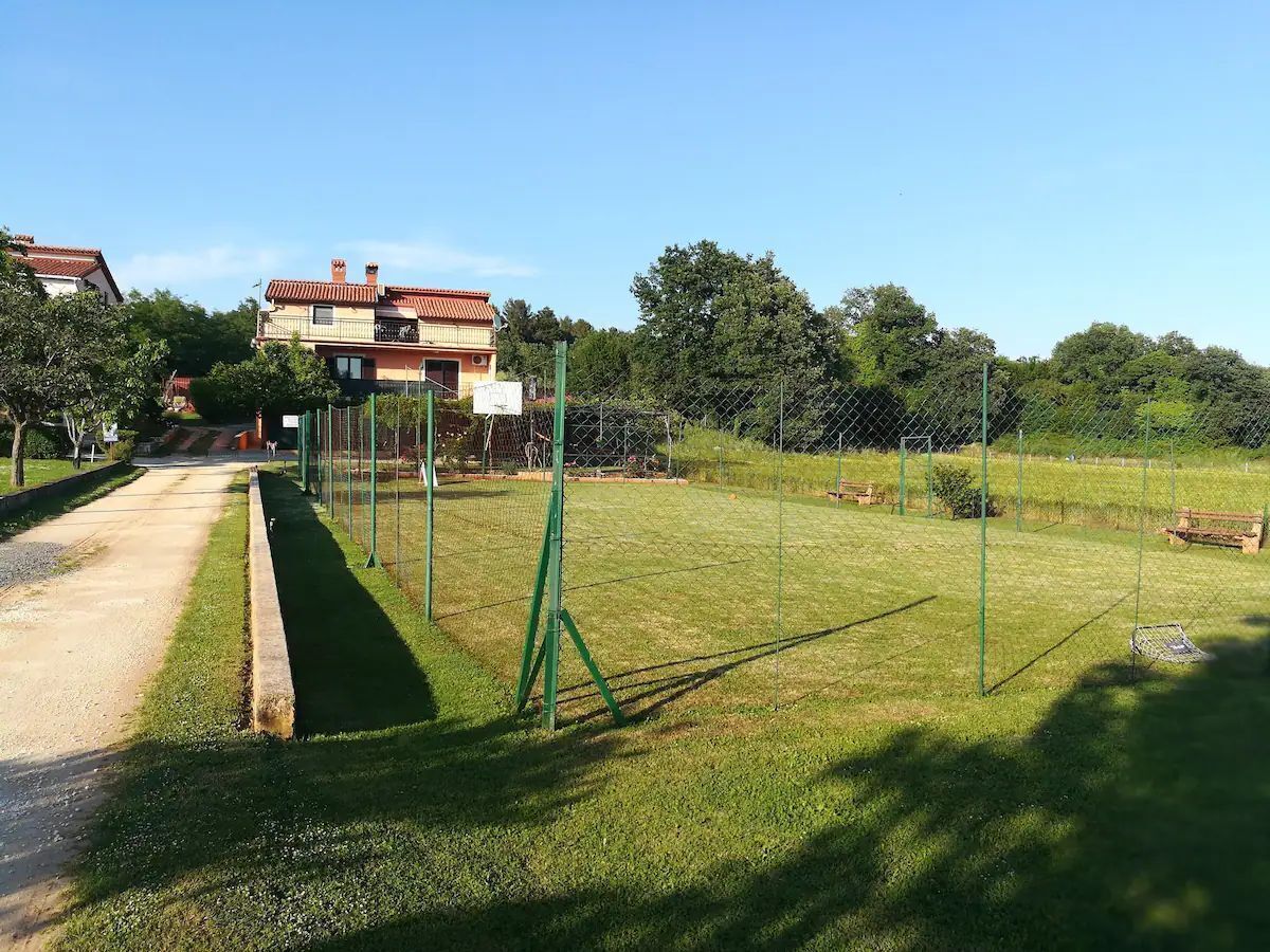 Un campo deportivo rodeado por una valla, con un camino despejado que lleva a un edificio.