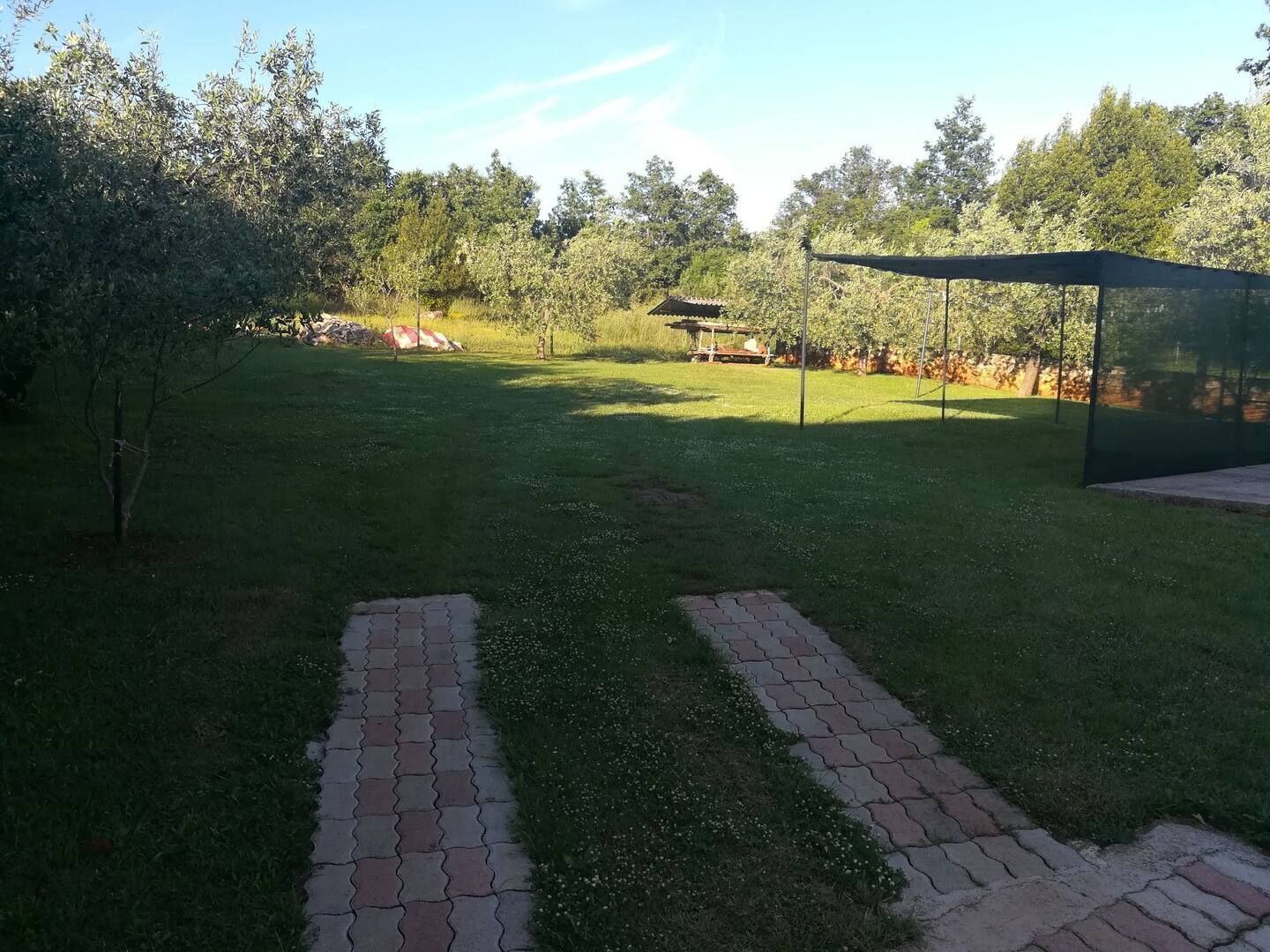 Un espacio al aire libre con césped y un sendero pavimentado que conduce a una zona cubierta con asientos.