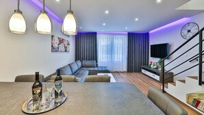 A modern living room with a sofa, dining table, and hanging pendant lights. - Apartment Silva (Split)