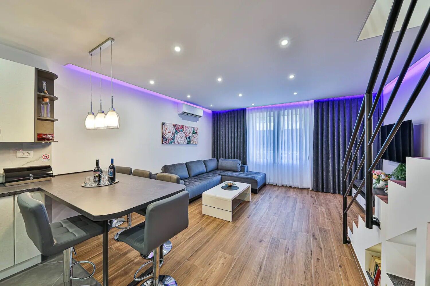 A modern living space with a dining area, sofa, and staircase.